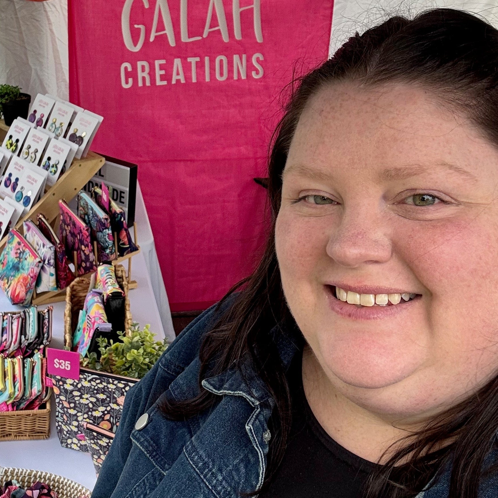 Woman standing in front of a stall with 'Little Galah Creations' branding, displaying various products.