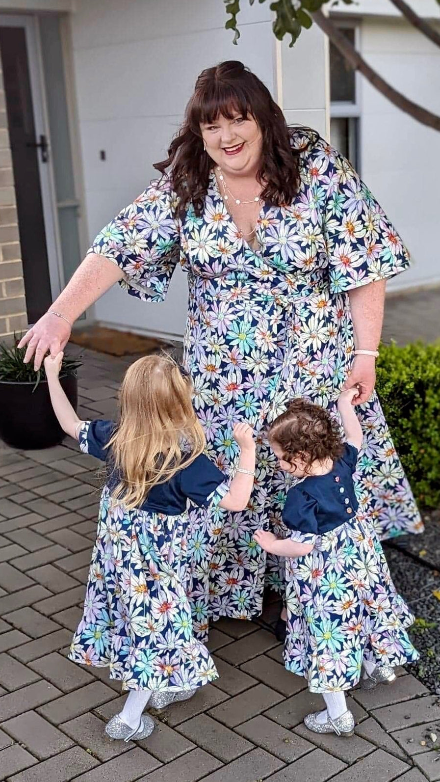 Woman and two children in matching floral dresses standing on a patio.