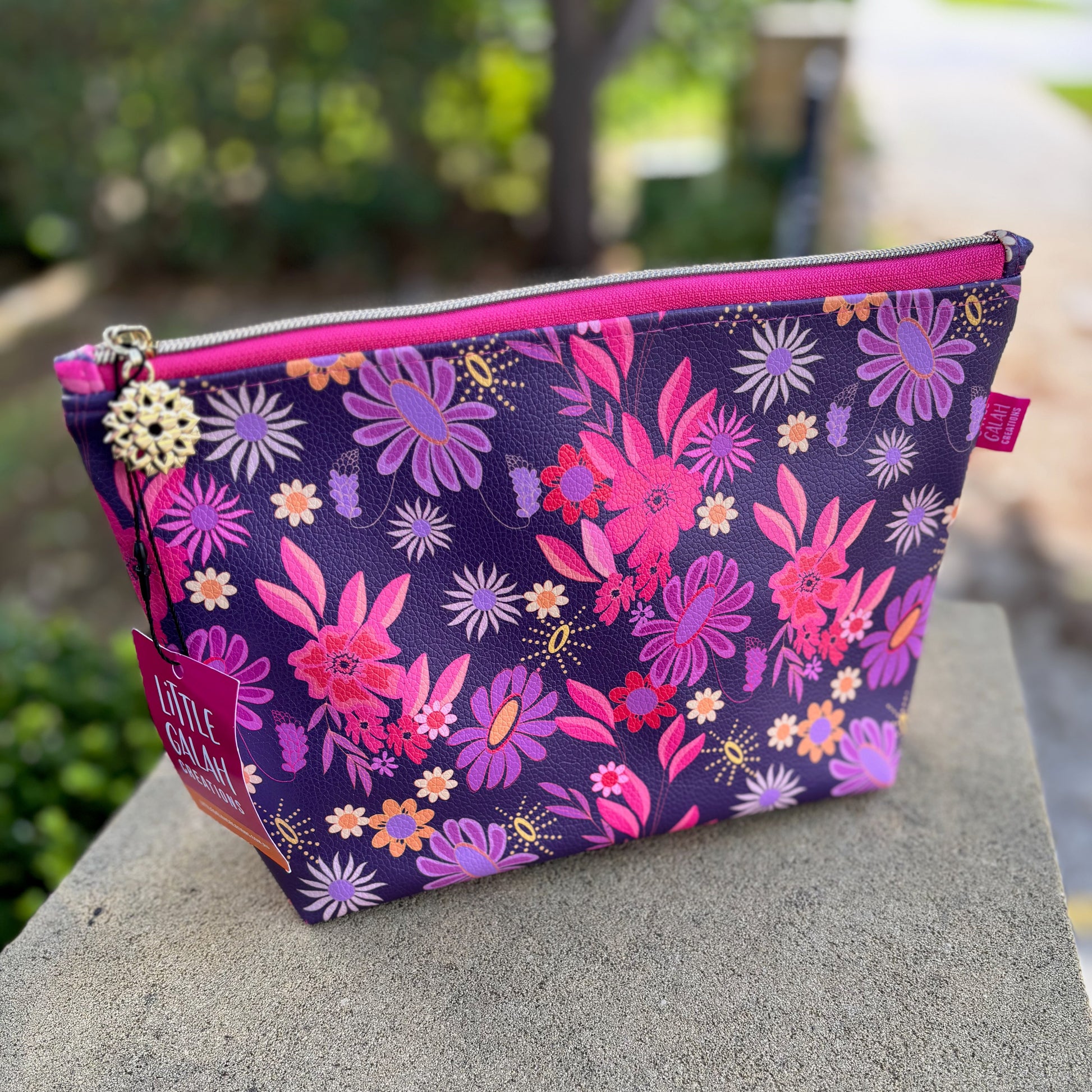 Floral-patterned pouch with pink zipper on a stone surface outdoors
