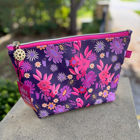 Floral-patterned pouch with pink zipper on a stone surface outdoors