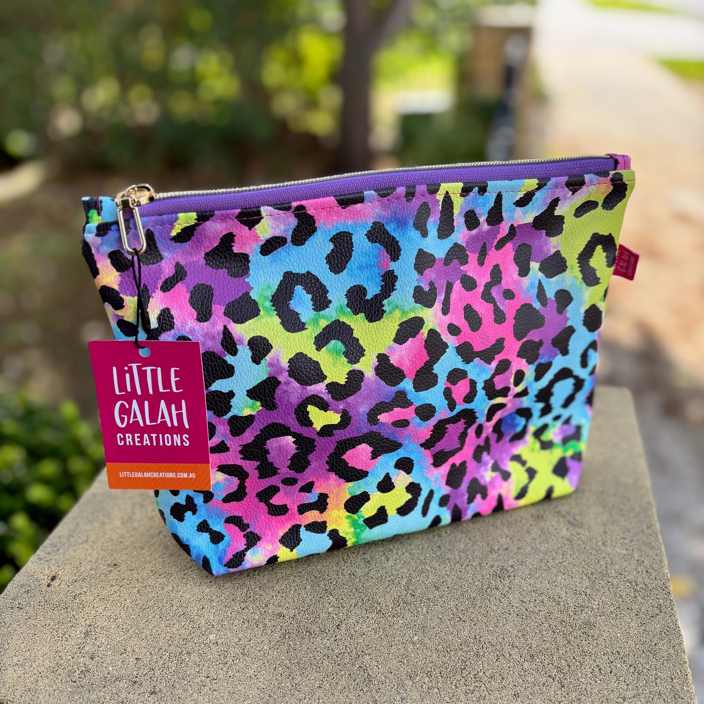 Colorful leopard print pouch with a 'Little Galah Creations' tag on a stone surface.
