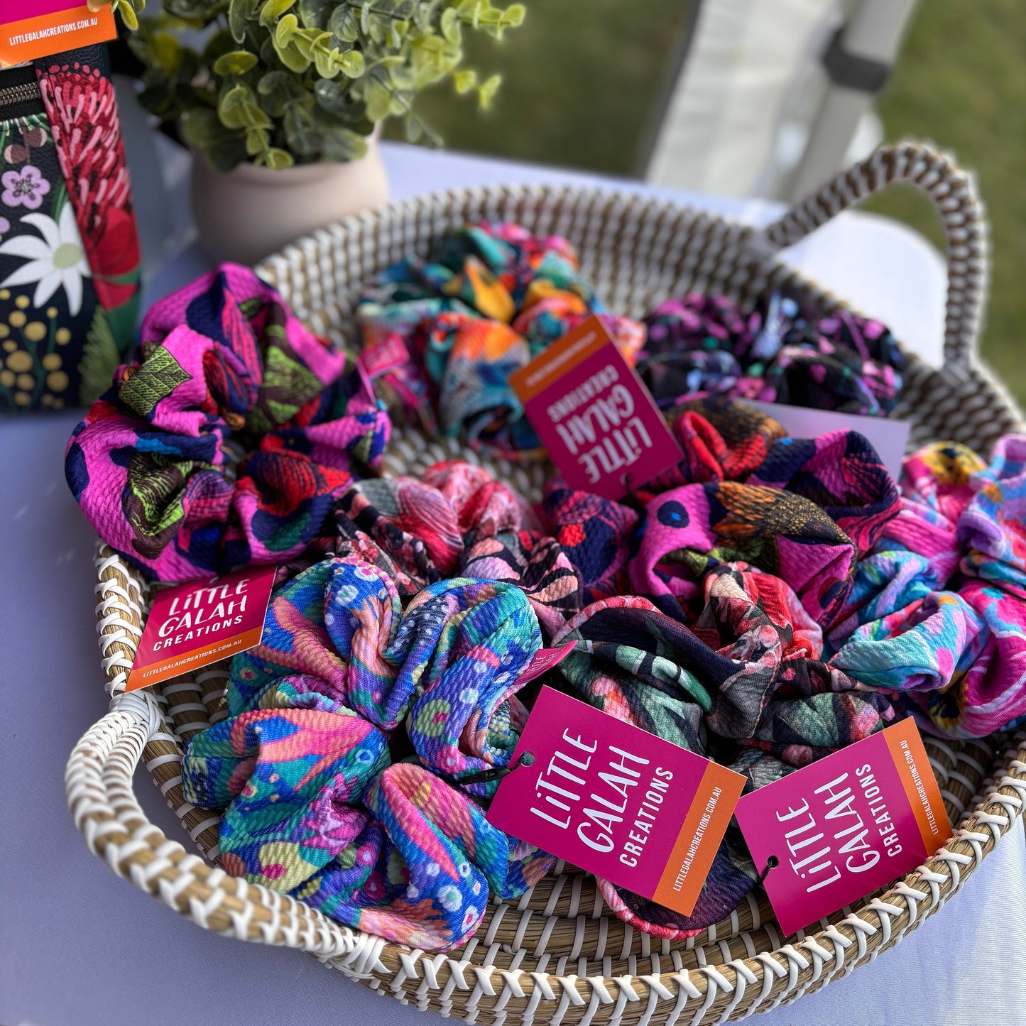 Colorful scrunchies in a woven basket with 'Little Galah Creations' tags.