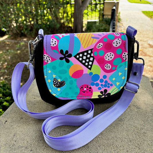 Colorful patterned handbag with a purple strap on a stone surface outdoors.
