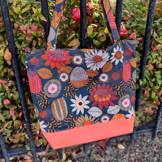 Floral patterned tote bag with a coral base hanging on a black metal fence.