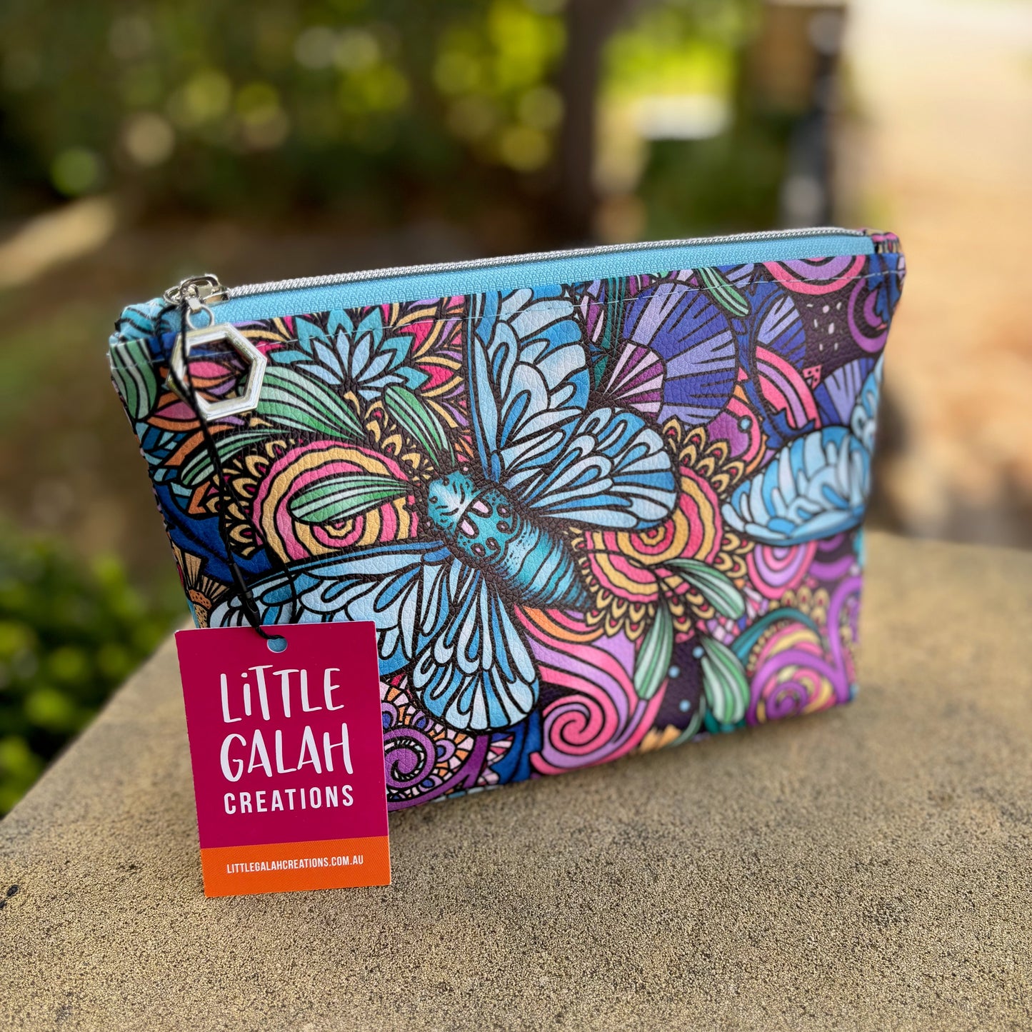 Colorful cicada-patterned pouch with a 'Little Galah Creations' tag on a stone surface.