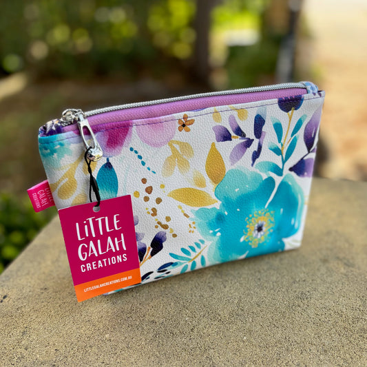 Floral pouch with 'Little Galah Creations' tag on a stone surface outdoors