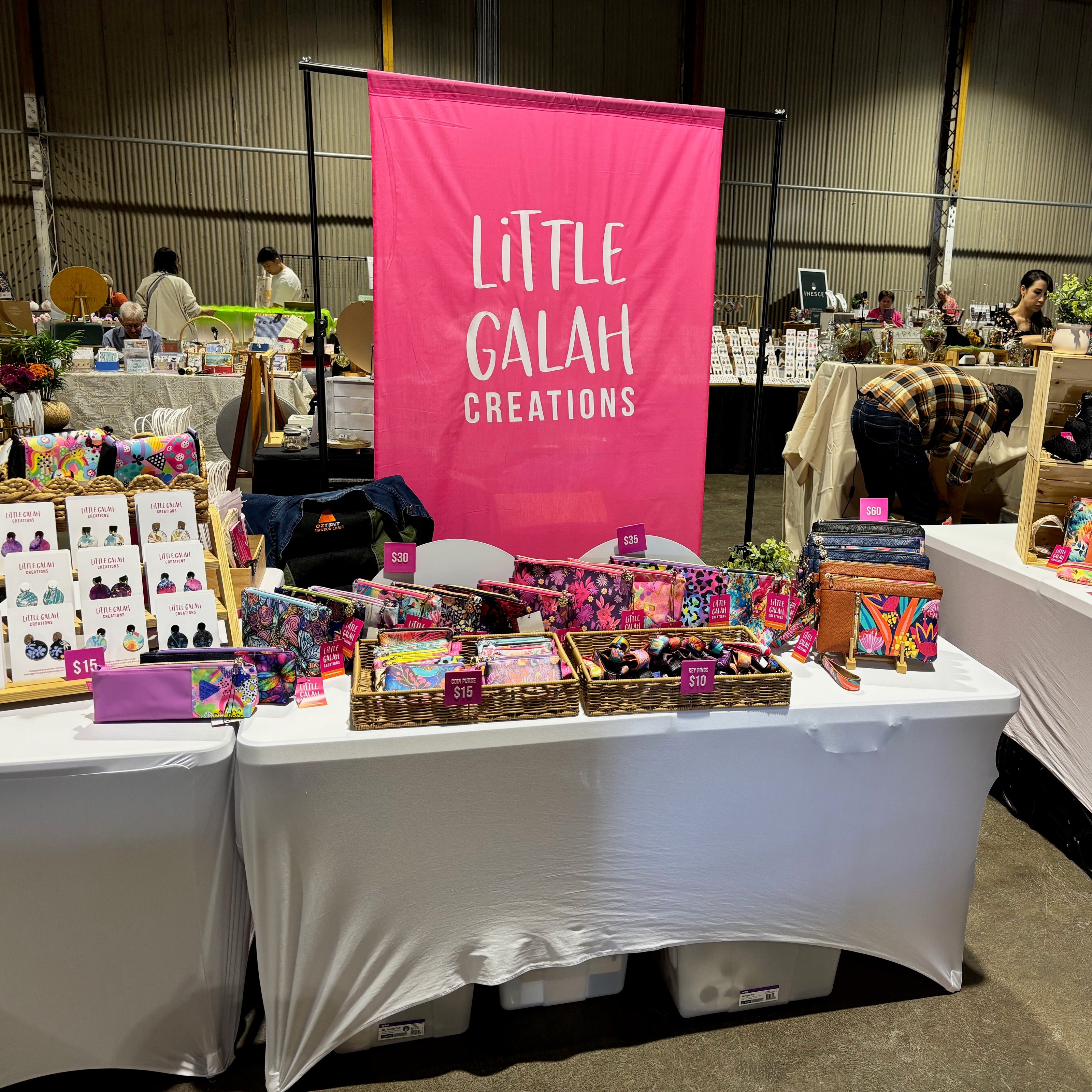 Table with 'Little Galah Creations' banner at a trade show or market.